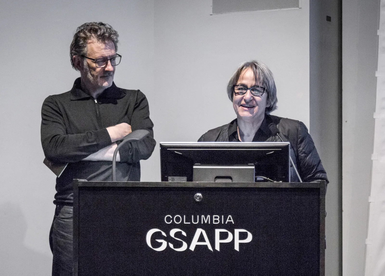 Anne Lacaton y Jean-Philippe Vassal en un atril durante una conferencia con la marca COLUMBIA GSAPP visible al fondo
