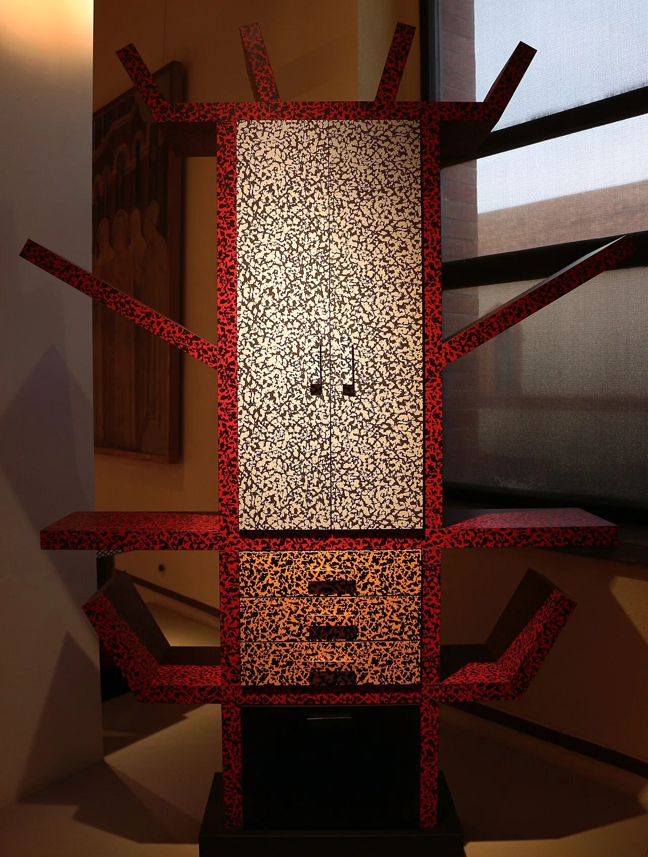 Casablanca, librería de Ettore Sottsass para Memphis 1981: estructura antropomórfica con brazos extendidos, panel central con doble puerta, cuerpo recubierto con laminado plástico decorado con patrón orgánico rojo y crema