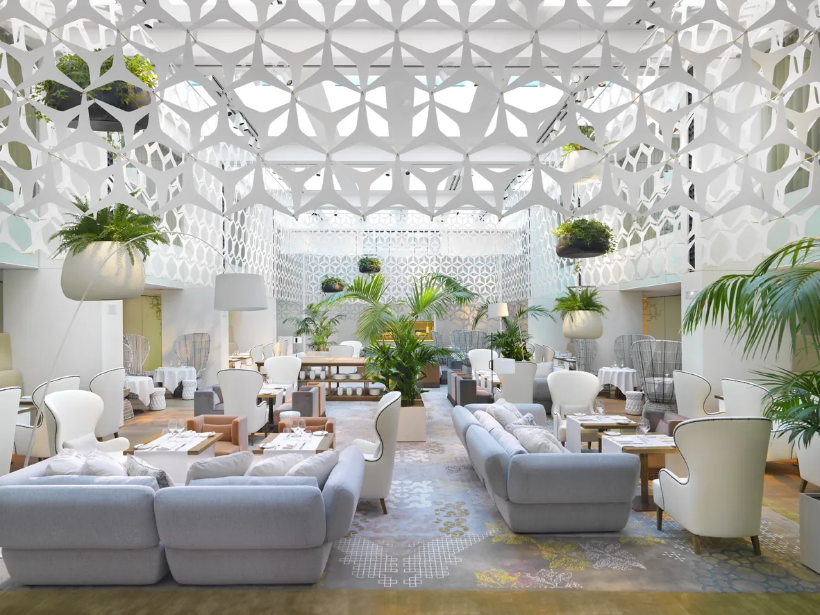 Restaurante Blanc del Mandarin Oriental Barcelona: patio interior cubierto con celosía geométrica blanca, sofás grises, butacas blancas con bordes negros, plantas tropicales colgantes y mesas con vajilla