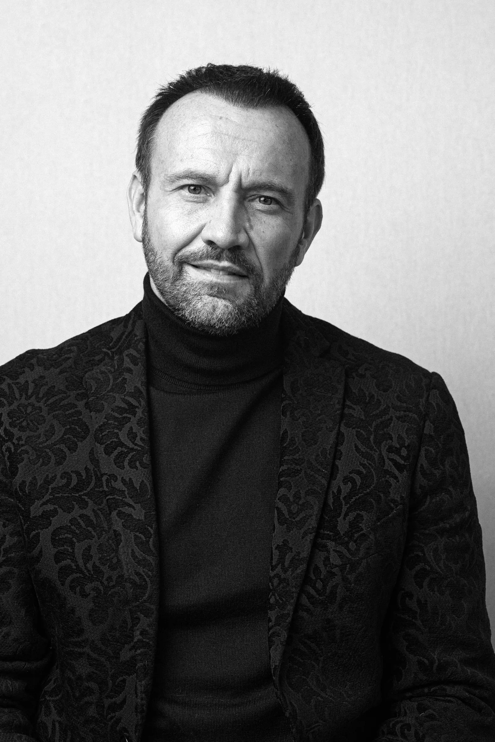 Retrato en blanco y negro de Mauro Porcini con jersey de cuello alto oscuro y chaqueta con estampado damasco sutil, mirada directa a cámara