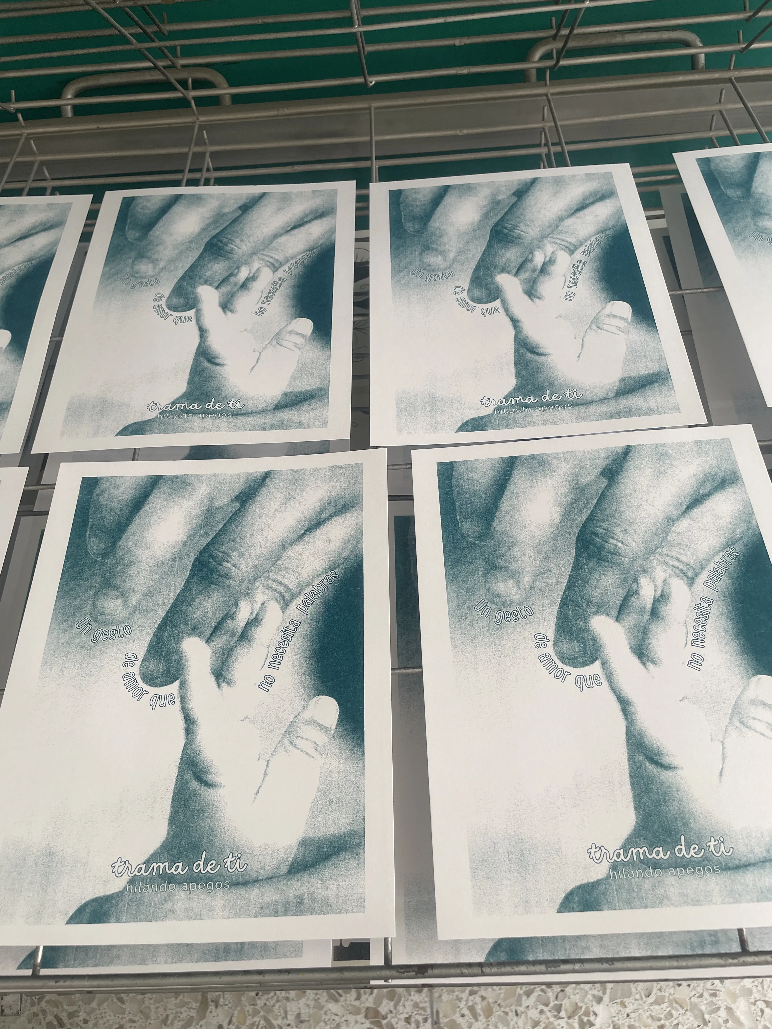 Pósters impresos con técnica risograph en tinta azul-petróleo: composición de manos sobre fondo blanco con texto al pie, granulado y textura característica del proceso visible en superficie