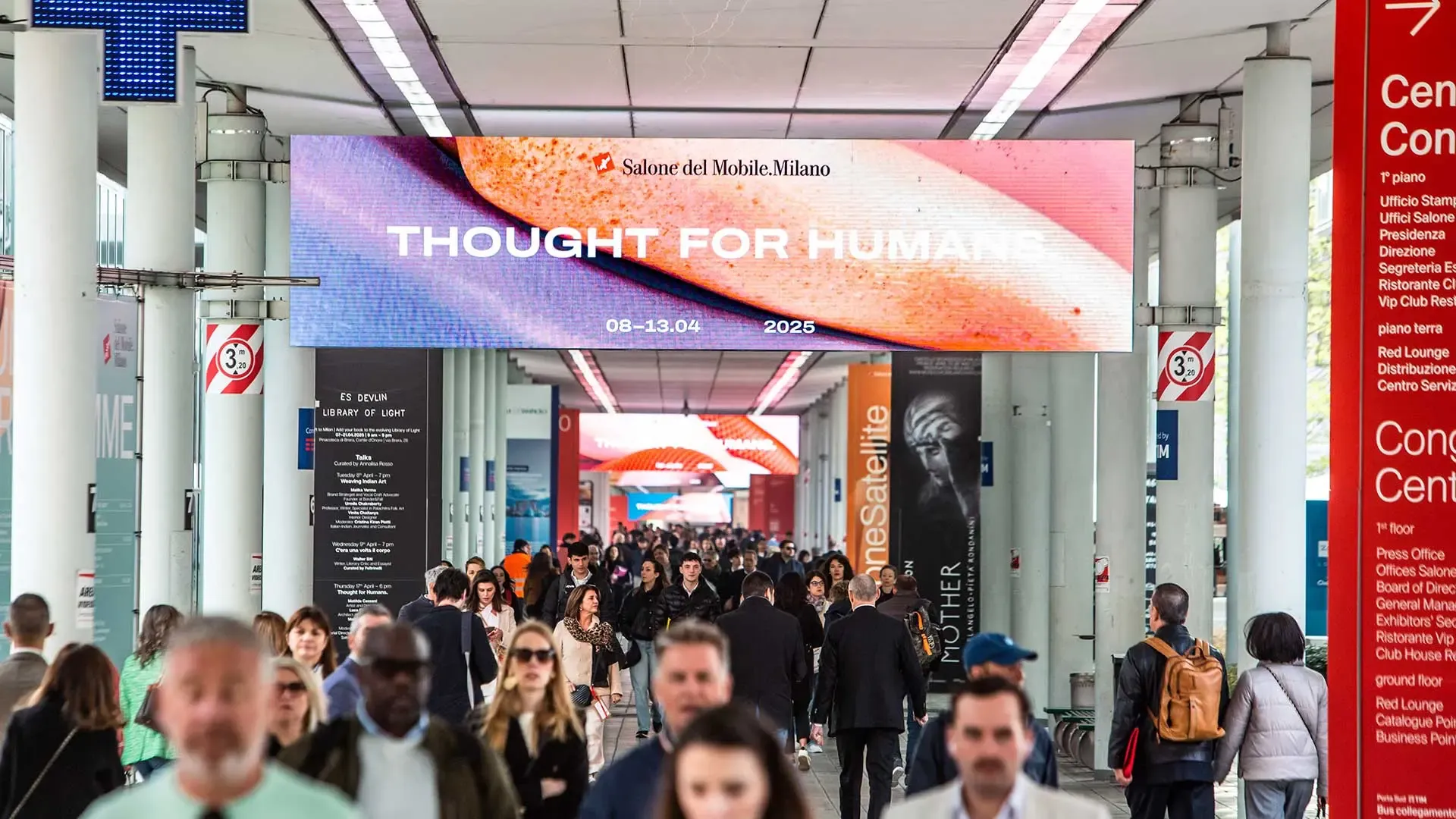 Vista interior del Salone del Mobile 2025 desde el acceso por Corso Italia: cartel digital con el lema 'Thought for Humans' y multitud de visitantes circulando por el pasillo principal