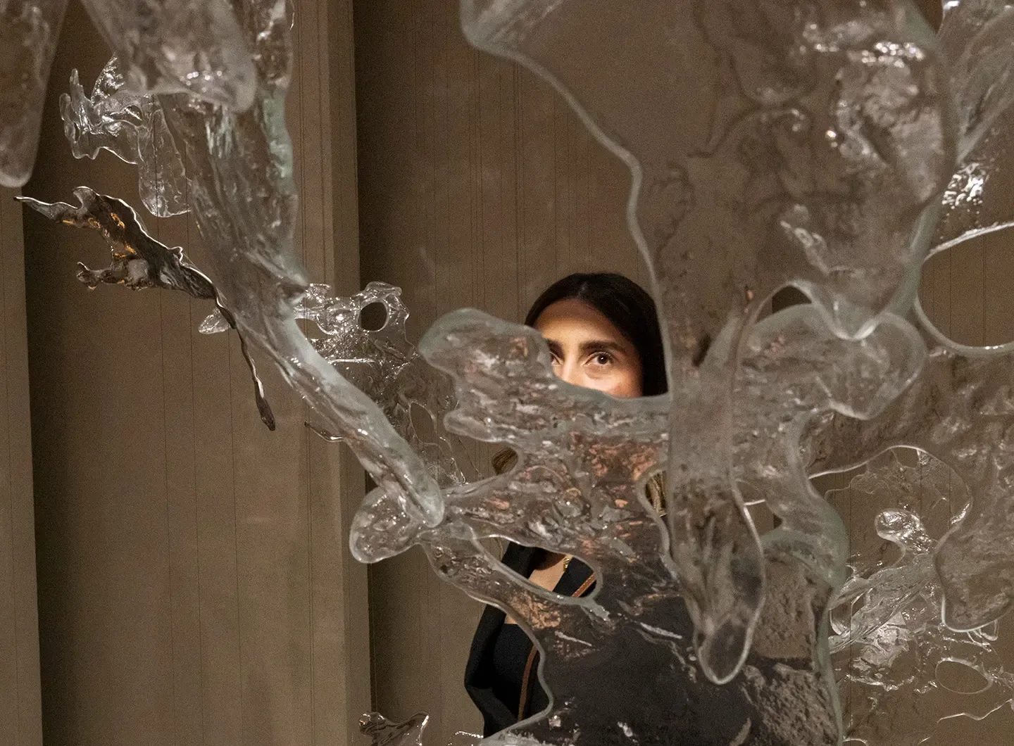 Pieza de cristal Splash de Lasvit en Euroluce 2025: forma orgánica de vidrio soplado retorcido evocando movimientos de agua, con el rostro de una visitante visible al fondo a través de la transparencia