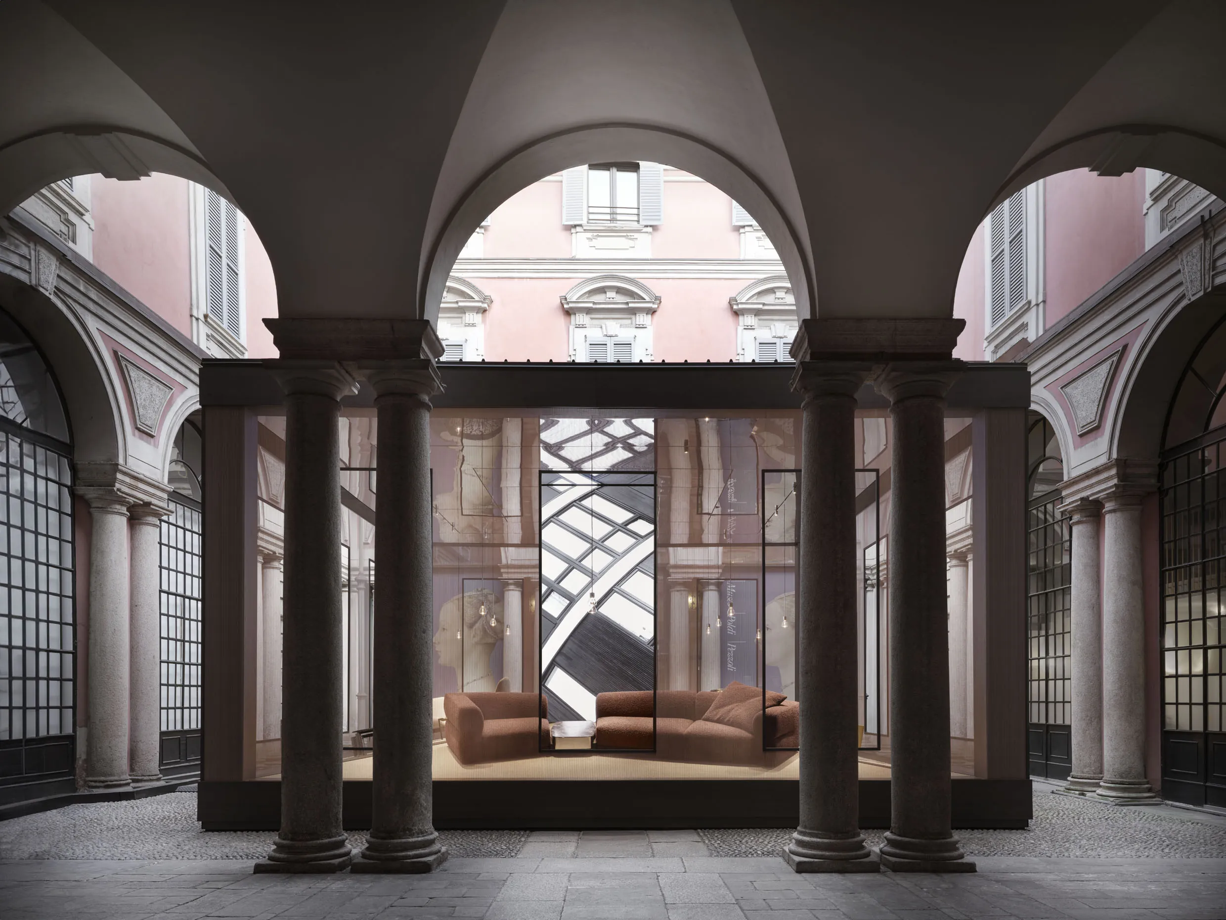 Instalación 'Letters to Milan' de Molteni&C en el patio del Museo Poldi Pezzoli: arcadas y columnas históricas con un sofá y estructura geométrica contemporánea integrada en el espacio