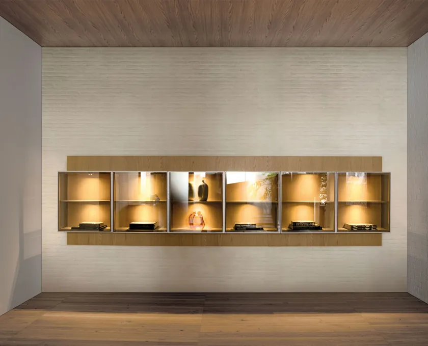 Sistema de almacenaje Pass-Word de Vincent Van Duysen para Molteni&C montado en pared: panel horizontal de madera con seis vitrinas iluminadas que contienen objetos curados, suelo de madera natural